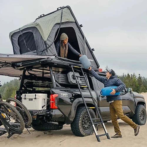Couple camping with Yakima SkyPeak HD rooftop tent, passing gear up ladder