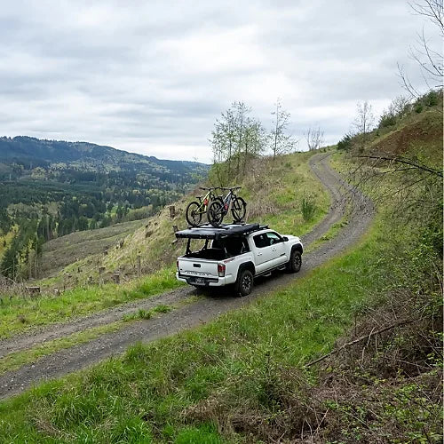 White Toyota Tacoma driving offroad trails with Yakima SkyPeak HD and mounted bikes